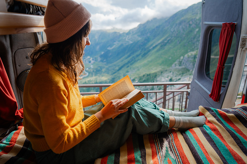 Woman reading book in camper van overlooking Furka Pass during trip to Swiss Alps
