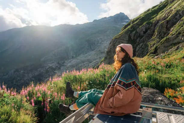 Serene woman sitting on rooftop of camper van overlooking Furka Pass