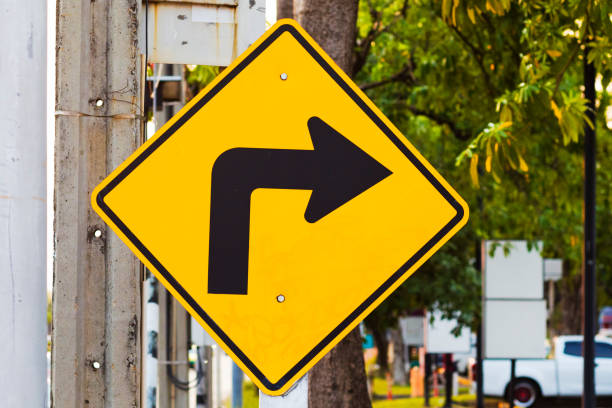 Yellow traffic sign with arrow left curve symbol beside the rural road to warn drivers to know the way ahead has right curve. Concept. Warning traffic sign for transportation.