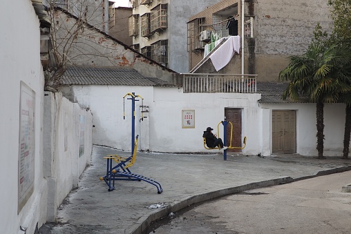 A lonely man sits on empty outdoor fitness equipment staring at his phone in a residential area of Xintao in China