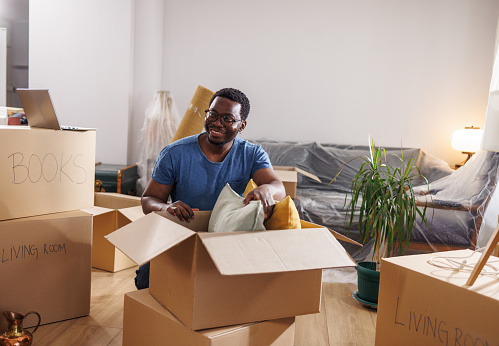 Young African American man unpacking stuff from the boxes in his new home