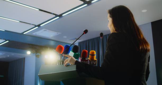 Female press officer pronounces speech from tribune during press campaign