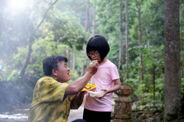An Asian grandfather and granddaughter spending time picnic at nature reserve forest