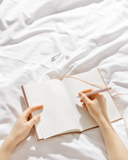 istock Woman makes plan, day results on blank white page diary journal on bed, writing in notebook or wish diary, holds notepad and pen in hands, Increasing mindfulness, relax and comfortable concept 2148294293