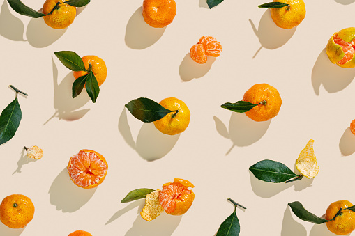 Fresh juicy orange yellow tangerines as minimal flat lay pattern, Sweet Citrus fruits with green leaves on beige table background. Still life geometric pattern of mandarin oranges overhead, above view