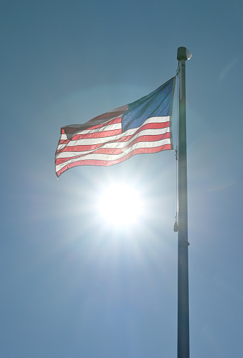 Sun shining behind waving American flag.