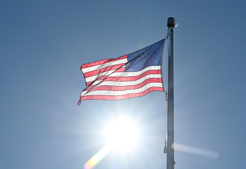 Sun shining behind waving American flag.