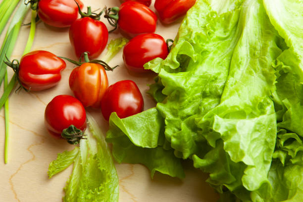 Fresh lettuce leaves and tomatoes on wood table, top view. Salad background from fresh vegetable for poster, calendar, post, screensaver, wallpaper, postcard, cover, website. High quality photography
