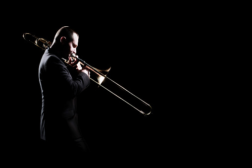 Trombone player. Trombonist playing jazz musician. Man playing brass instrument isolated on black