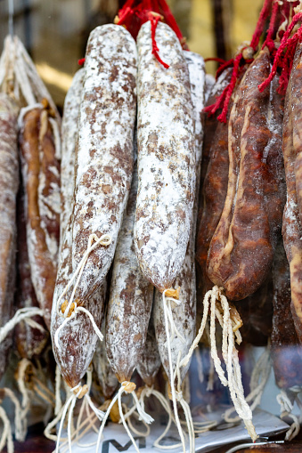 Spanish salami, fuet and salchichón sausages hang on a shelf against a black background.