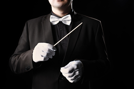 Orchestra conductor hands closeup music conducting. Man with baton in white gloves and bowtie close up