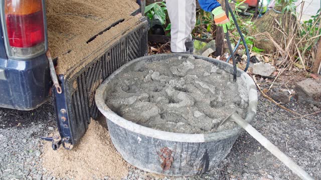 Worker uses a hose to add water to a basin and Mixing Cement and Sand, Construction Site and Building Materials concept.