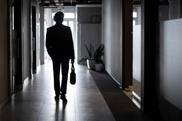 silhouette eines geschäftsmannes in voller größe, ein mann im büro geht den flur entlang, unternehmen, ein angestellter im business-anzug - abschied stock-fotos und bilder