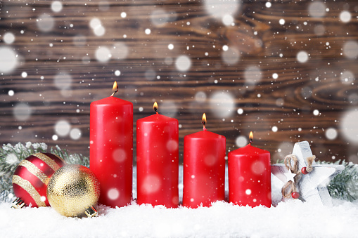 Christmas candles with ornaments and white snow on brown wooden background