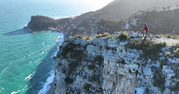 Aerial view of mature man on electric mountain bike on cliff above sea,  Liguria