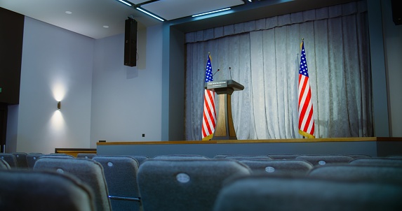 Tribune for the presidential candidate of the United States political speech in the White House. Press campaign room with seats and American flags. Conference debate stand with microphones on stage.