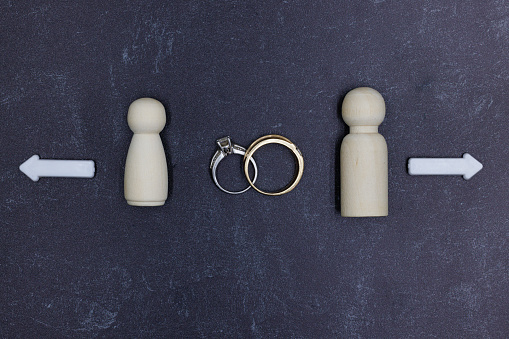 Married Man and Woman Wooden Figurines Experiencing Divorce Separation with white arrows and wedding rings on a slate counter.