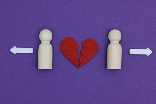 Two Married Men Wooden Figurines Experiencing Divorce Separation with white arrows and broken heart on purple background