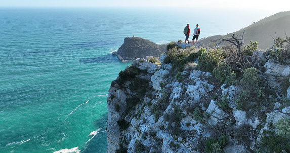 Aerial view of mature couple hiking on cliff above sea,  Liguria