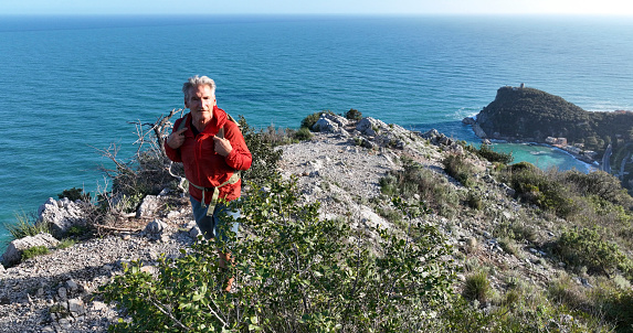 Aerial view of mature hiker on cliff above sea,  Liguria
