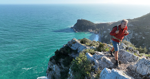Aerial view of mature hiker on cliff above sea,  Liguria