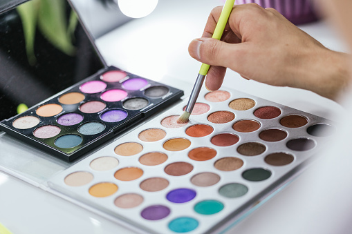 Close-up photo of an unrecognizable person using a colorful make-up palette in backstage