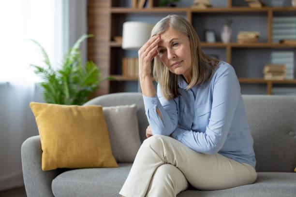 istock Thoughtful elderly lady sitting cross legged and resting head on hand with frustrated expression.Tired woman suffering from headache while rubbing forehead and looking forward with disappointment 2148300923