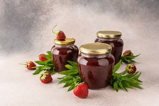 Homemade summer preservation, strawberry jam in jars, jars with jam and mint leaves and fresh strawberries