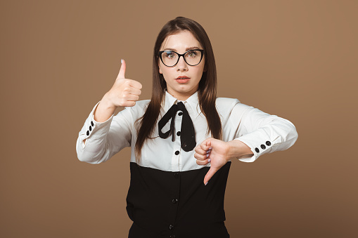 Puzzled Beautiful Young Woman Gesturing with Confusion, Expressing Dilemma, Simultaneously Showing Thumbs Up and Thumbs Down. Conceptual Photo Illustrating Indecision, Ambivalence, and Mixed Emotions