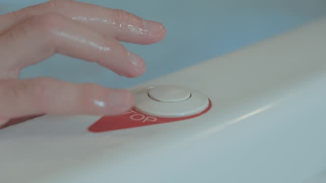 A hand presses the stop button of the hot tub