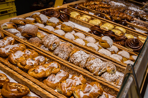 A lot of sweet pastries in baskets on the counter in the food store. Bakery on the buffet table. Business breakfasts and catering at events. Various bread type on shelf. Close-up. Selective focus.