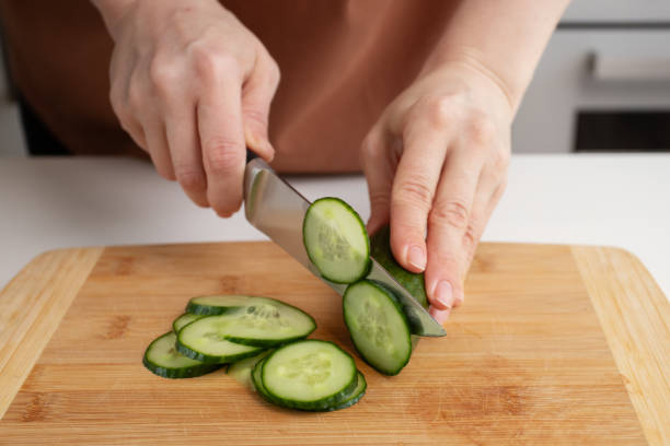 istock Woman's hand cutting cucumbers, kitchen cooking, vegetable slicing, salad preparation. 2148304731