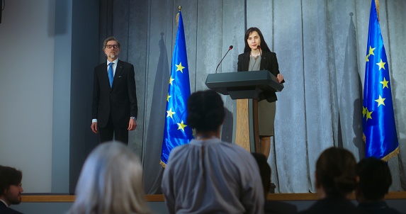 Female politician comes to tribune, delivers campaign speech, answers journalists questions, gives interview to media. Representative of the European Union performs at press conference. Elections day.