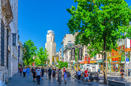 Antwerp, Belgium, July 7, 2023: crowd of people tourists walking down pedestrian shopping street with many multi-brand stores and shops, Boerentoren Farmers Tower KBC Tower building background