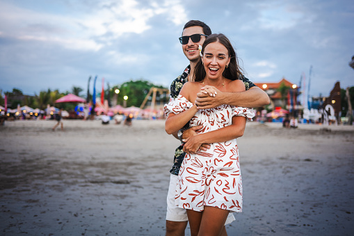 Happy couple having fun while cuddling on the sunset beach at Bali island.