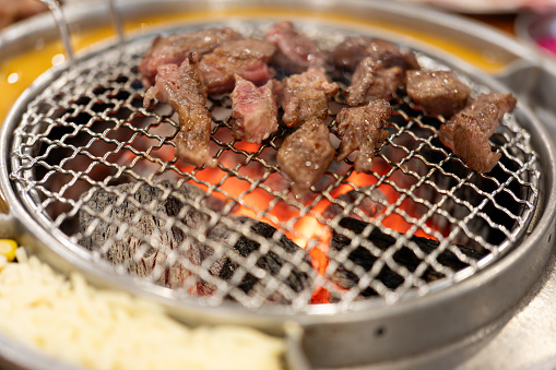 In the barbecue restaurant, the waiter lays a barbecue net on the red environmentally friendly barbecue charcoal, and uses food tongs to place the steak and bones, teaching delicious and juicy barbecue food cooking