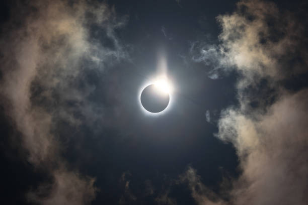 éclipse solaire totale du 8 avril 2024 avec le soleil culminant derrière la lune en train de créer. un effet bague diamant. totalité avec couronne brillante visible sur un ciel bleu foncé avec quelques nuages. - éclipse solaire totale photos et images de collection