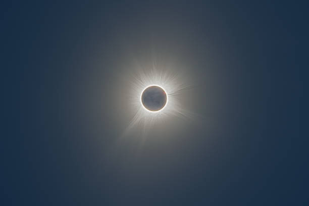 Total solar eclipse of April 8th 2024 with the sun peaking from behind the moon creating. a diamond ring effect. Totality with bright corona visible against dark blue sky with a few clouds.