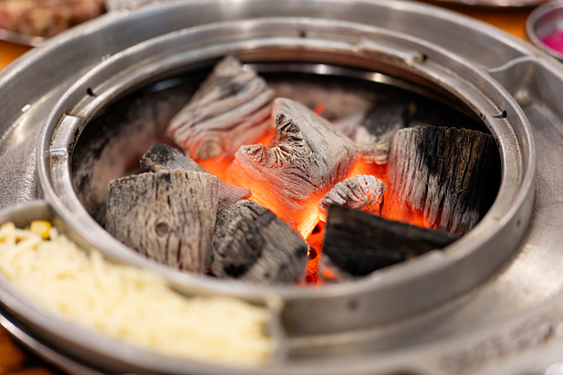 Hot red charcoal is placed under the Korean barbecue grill, with cheese, eggs, pork and beef next to it