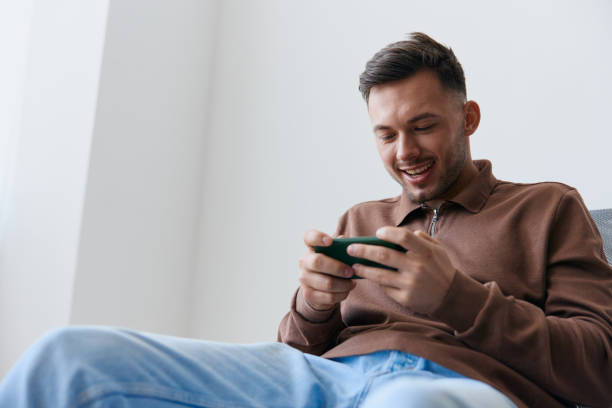 istock Cool RPG game offer. Mobile App concept. Enjoyed mission attractive smiling cheerful playing in good raising opening mouth looks at screen. Happy guy relaxing with phone chatting with friends 2148309167