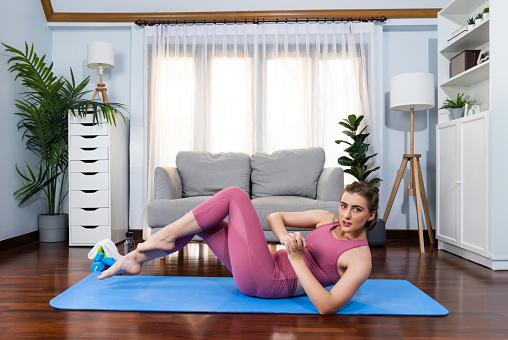 Athletic and sporty woman doing crunch on fitness mat during home body workout exercise session for fit physique and healthy sport lifestyle at home. Gaiety home exercise workout training concept.