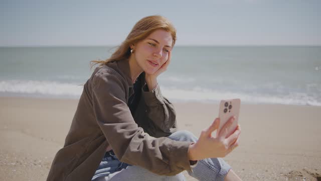 beautiful red-haired young woman takes a selfie or broadcasts on her social network how she is enjoying herself on a tropical beach on a deserted tropical beach near the ocean or sea