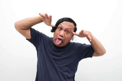 close-up portrait of Asian man glaring or ugly face and looking at camera. portrait of Indonesian man in dark blue shirt on isolated white background. a mocking facial expression or a silly face