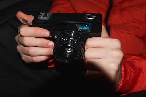Close-up of 35mm film camera held in hands. Classic model from the 90s, with a black body and lens. The photo captures the nostalgia of film photography and the excitement of capturing moment in time.
