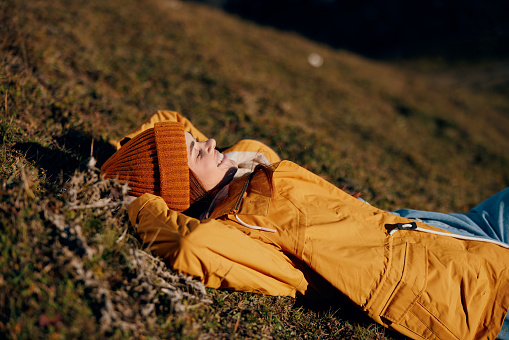 Woman beautifully lying on a hill recreation smile with teeth in the mountains in the autumn in a yellow raincoat and jeans happy sunset trip to hike the mountains in the snow, freedom lifestyle . High quality photo