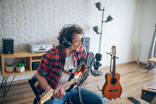 Guitar player recording music with condenser microphone in a home studio