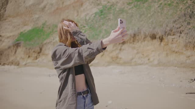 beautiful red-haired young woman takes a selfie on a deserted tropical beach near the ocean or sea