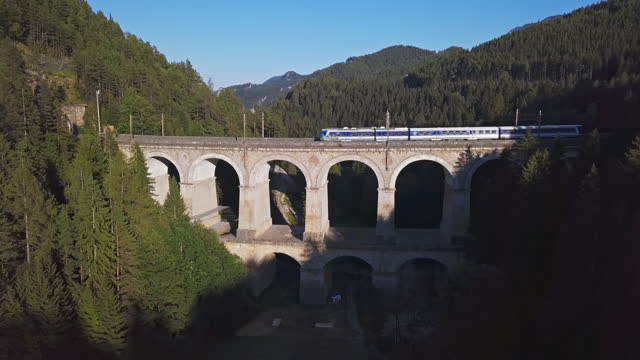 Aerial view of passenger train rides on historical Semmering mountain railway (Semmeringbahn) and famous Kalte Rinne Viaduct, Lower Austria.