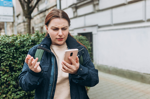 Upset sad, skeptical, serious woman holding smartphone gadget for communicate outdoors. Negative people emotion, Urban lifestyle concept. Angry 30s girl reading bad news