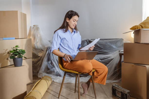 istock Young woman using laptop in new home and holding documents 2148320733